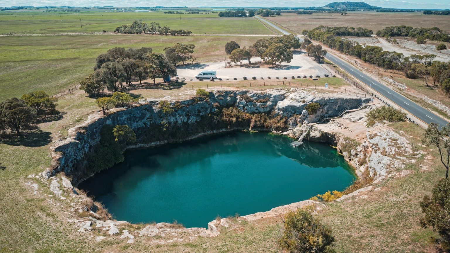 Aerial view of a deep blue sinkhole lake amid farmland, Little Blue Lake, Mount Gambier, South Australia