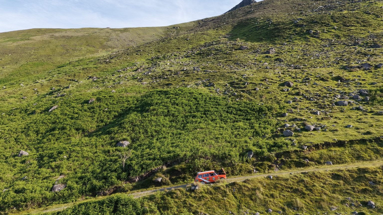 Aerial view of a rally car on a track across green mountain slopes