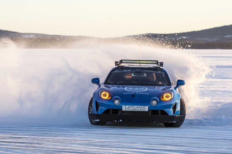 Blue Alpine sports car drifting on ice, spraying snow, hills in the distance