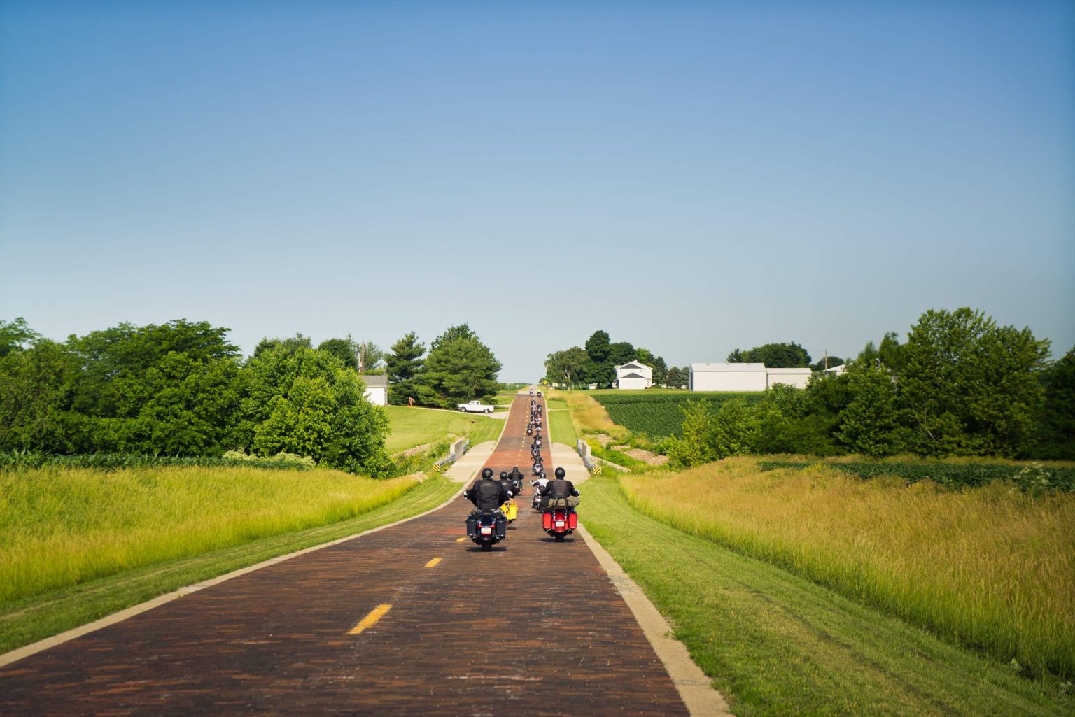 Motorcyclists riding a red brick section of old Route 66 through green fields