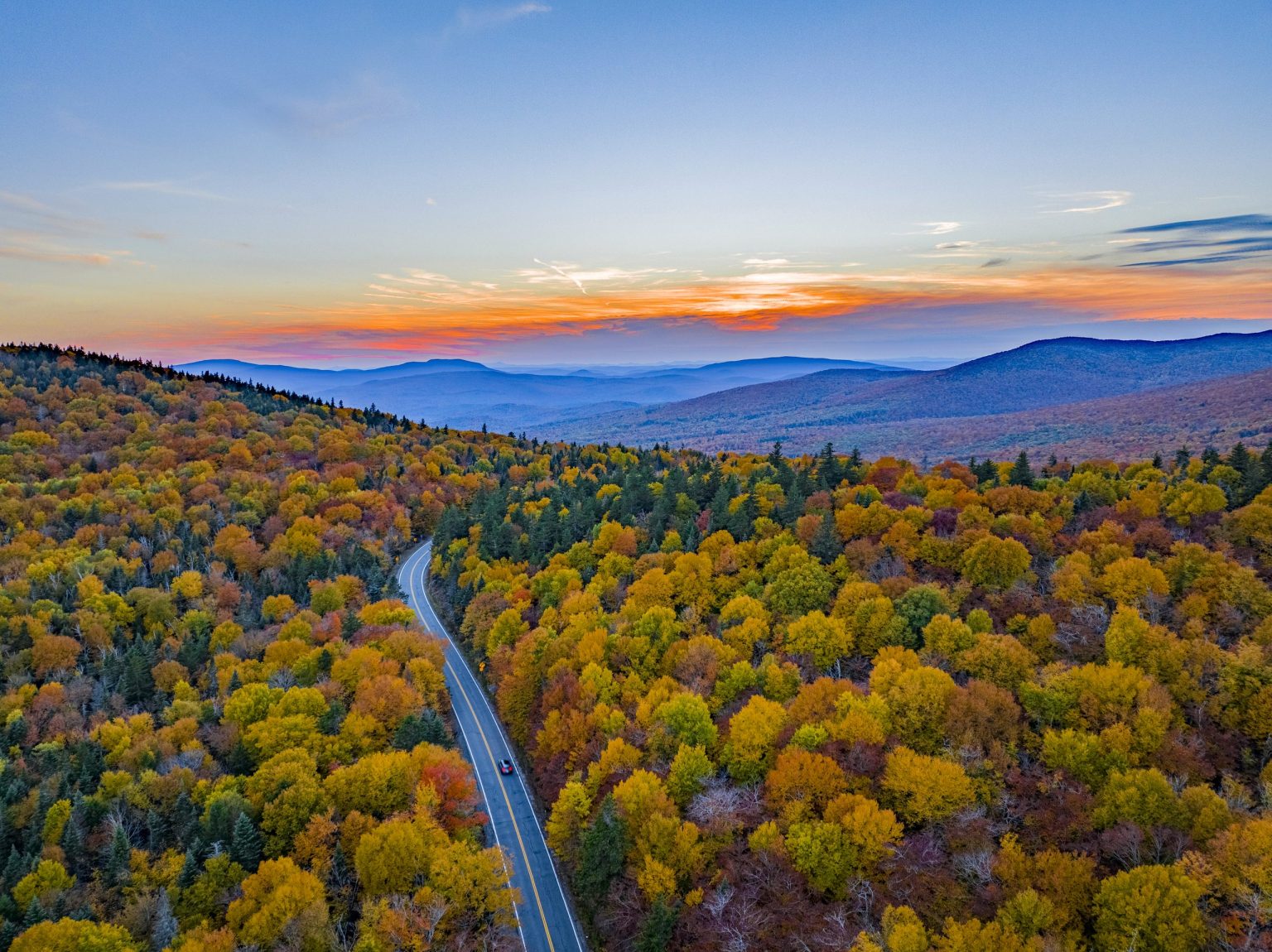 Road through autumn forest in New England at sunset
