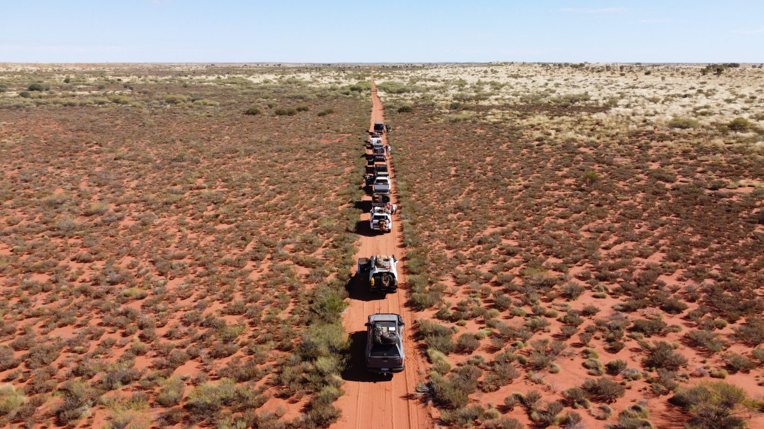 Line of 4x4s on a straight red track across the outback