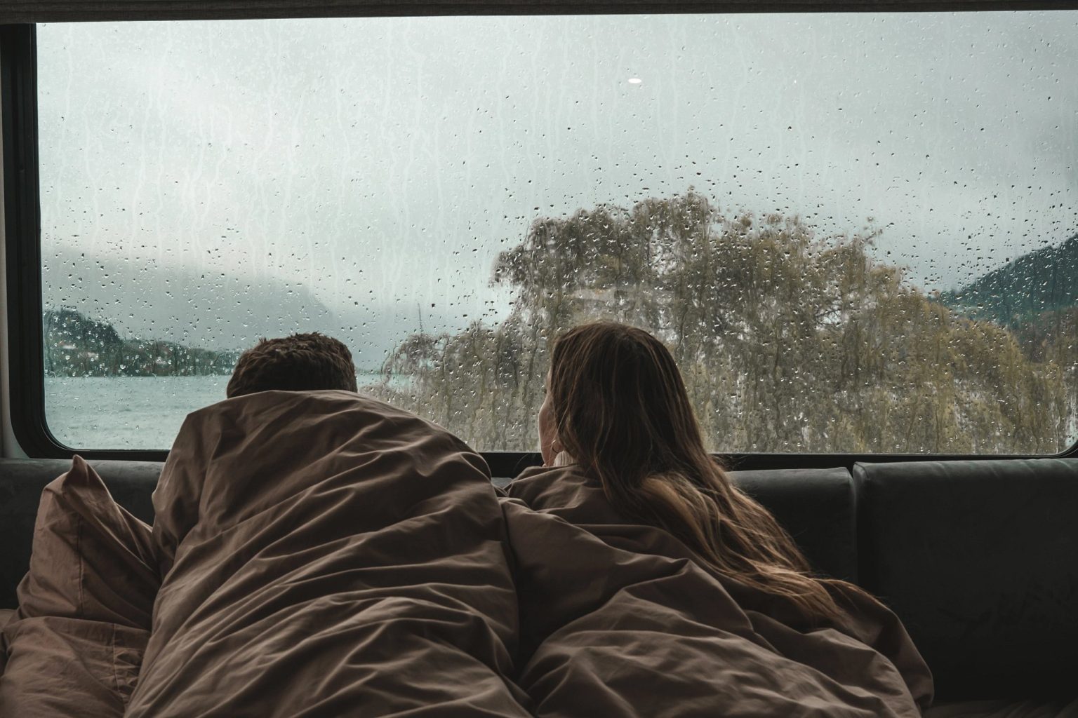 Couple wrapped in blankets watching rain on the window, Queenstown, New Zealand's South Island