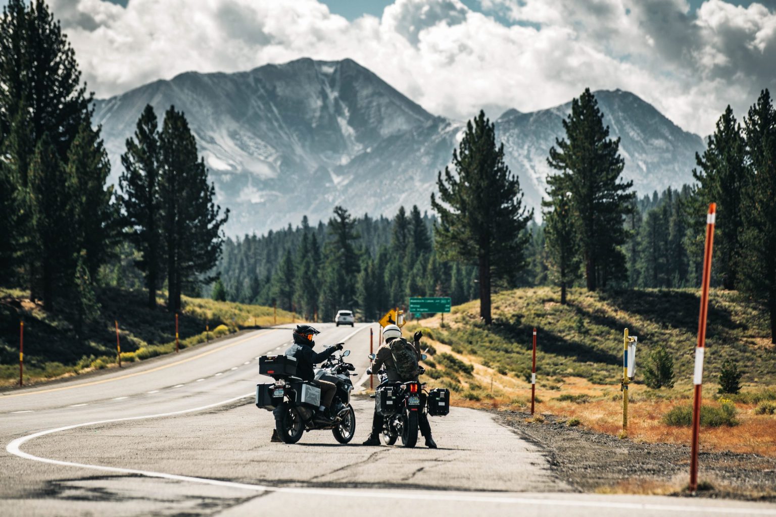 Two adventure motorcyclists stopped at a mountain roadside in the Colorado Rockies