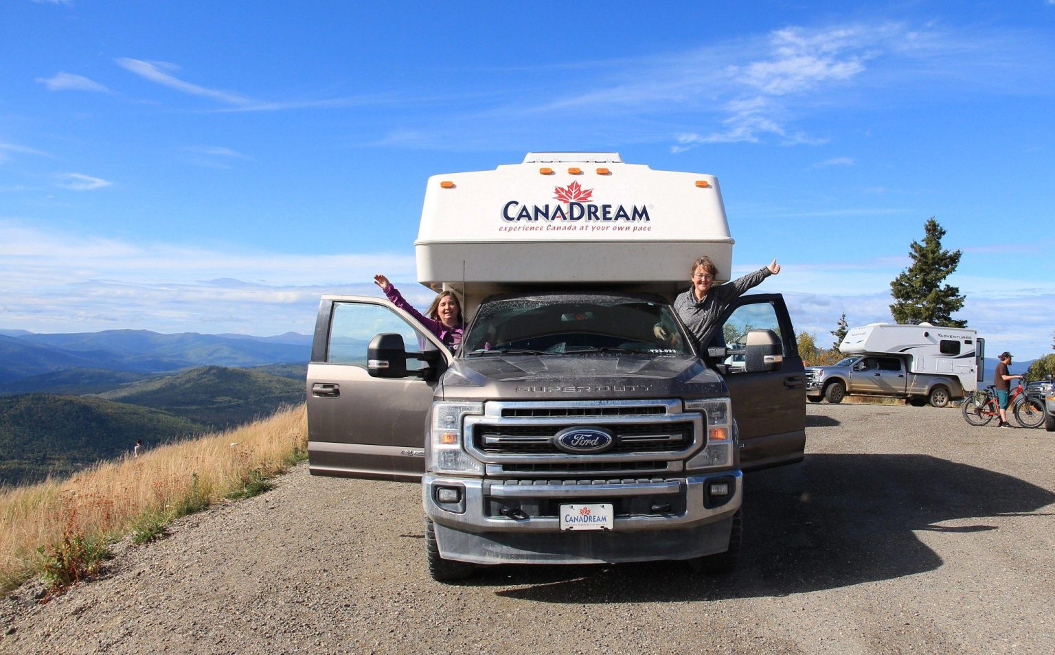 Couple waving from a truck camper on a mountain road, Canada
