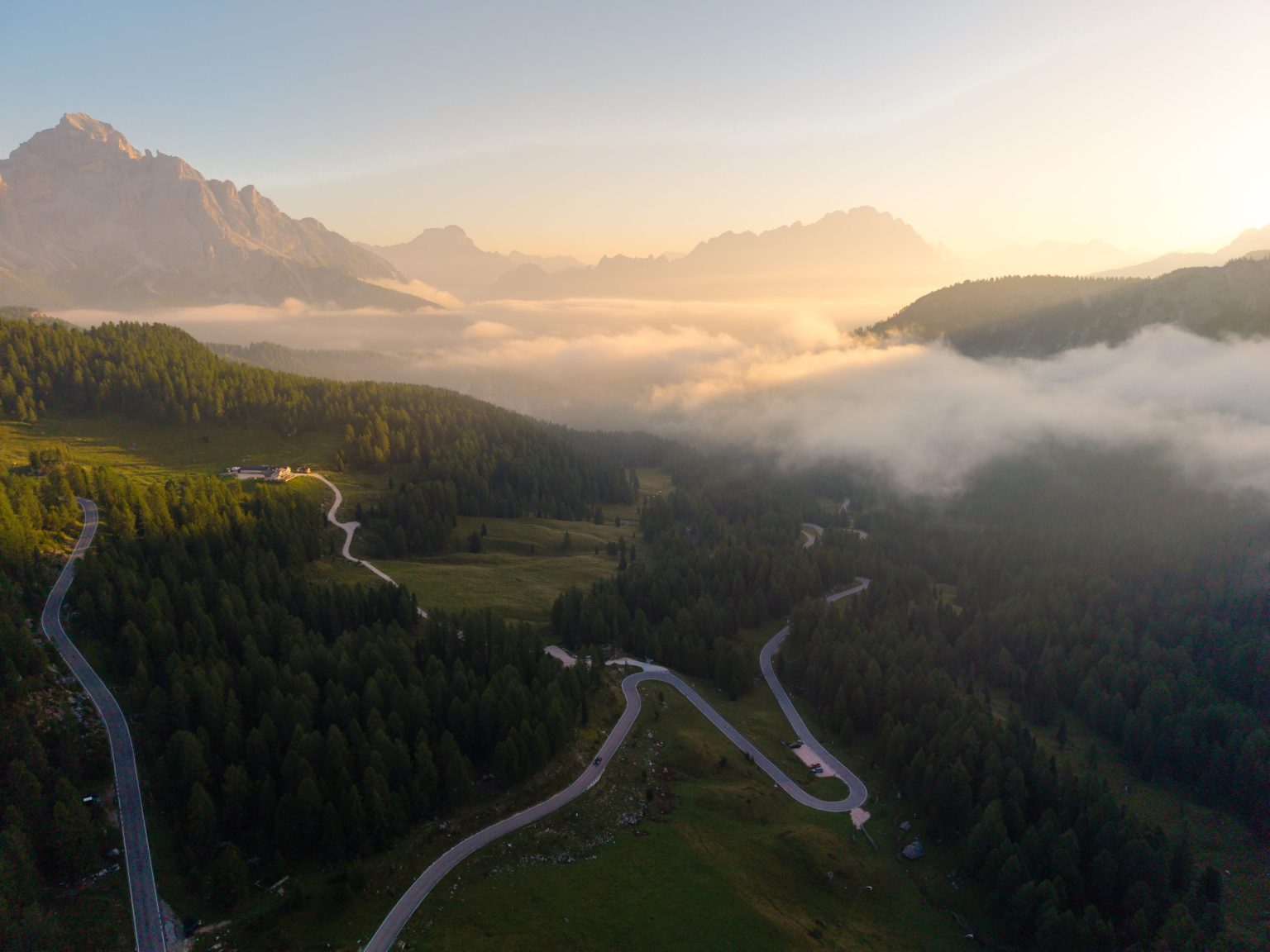 Road winding through forest towards Dolomite peaks at sunrise