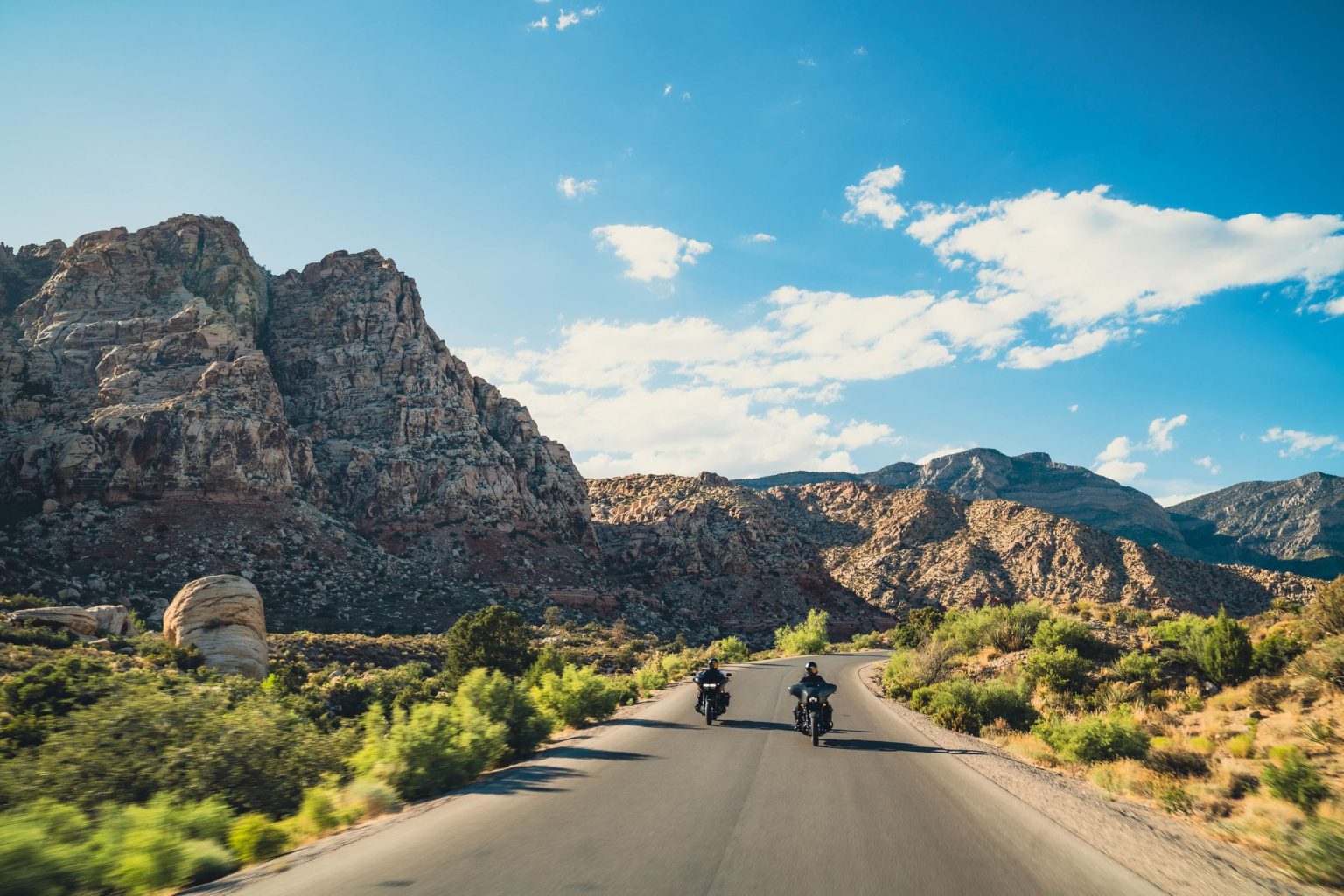 Two motorcyclists riding a desert road through red rock mountains near Las Vegas