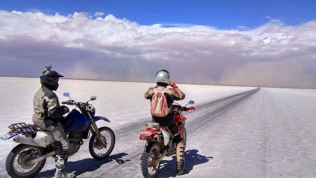 Two riders on motorcycles stopped on a white salt flat with a track ahead