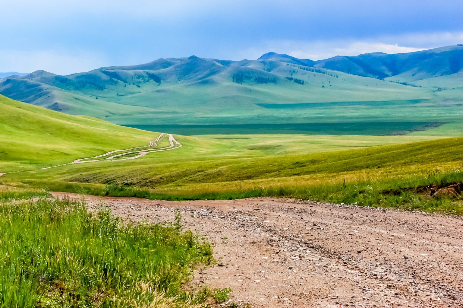 Dirt track winding through the rolling hills of the central Mongolian steppe