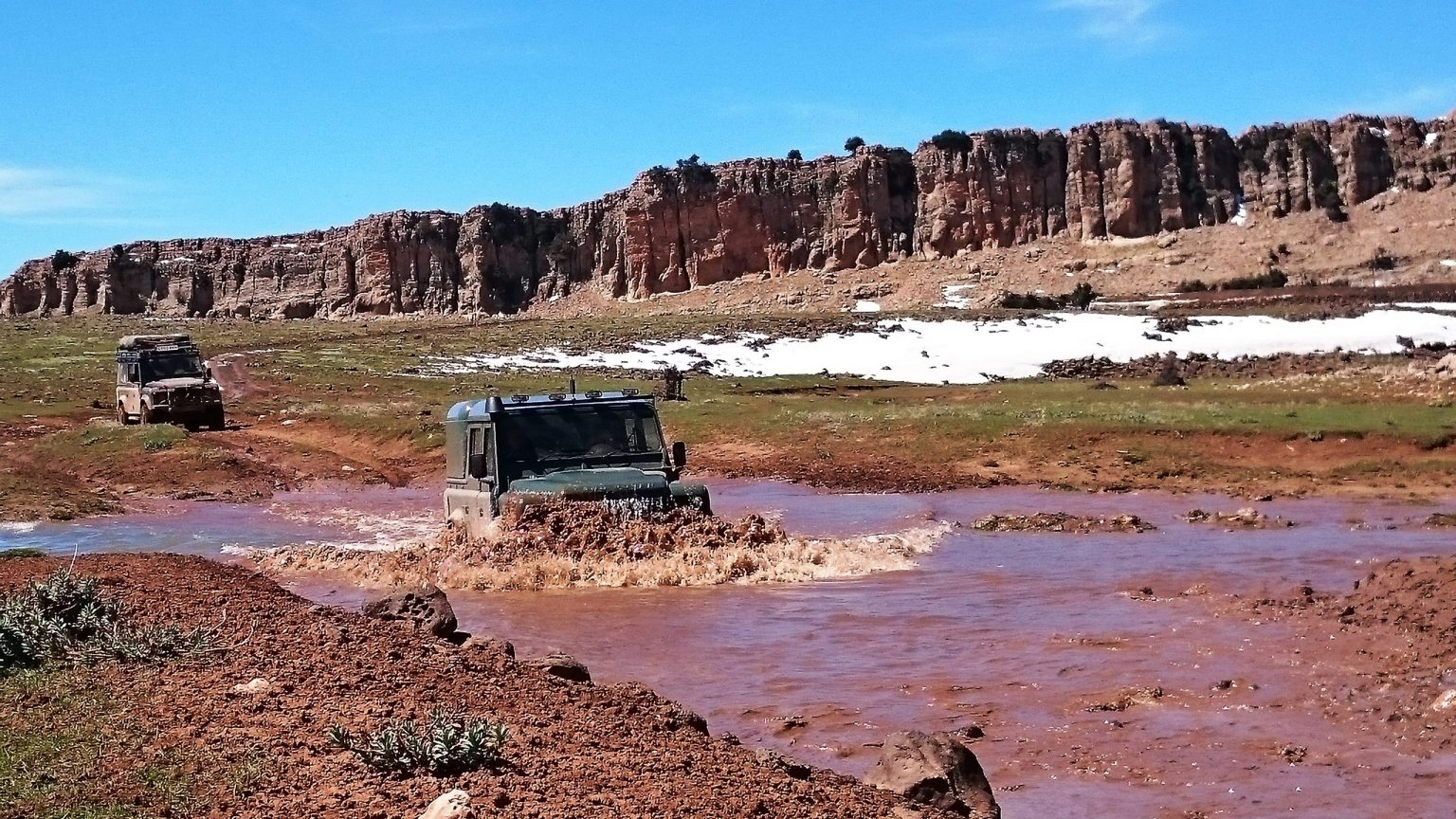 4x4 splashing through a river below red cliffs in Morocco
