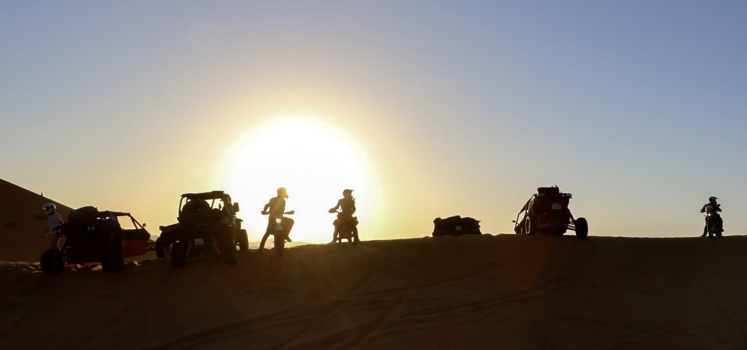 Riders silhouetted against the sun setting over the Sahara