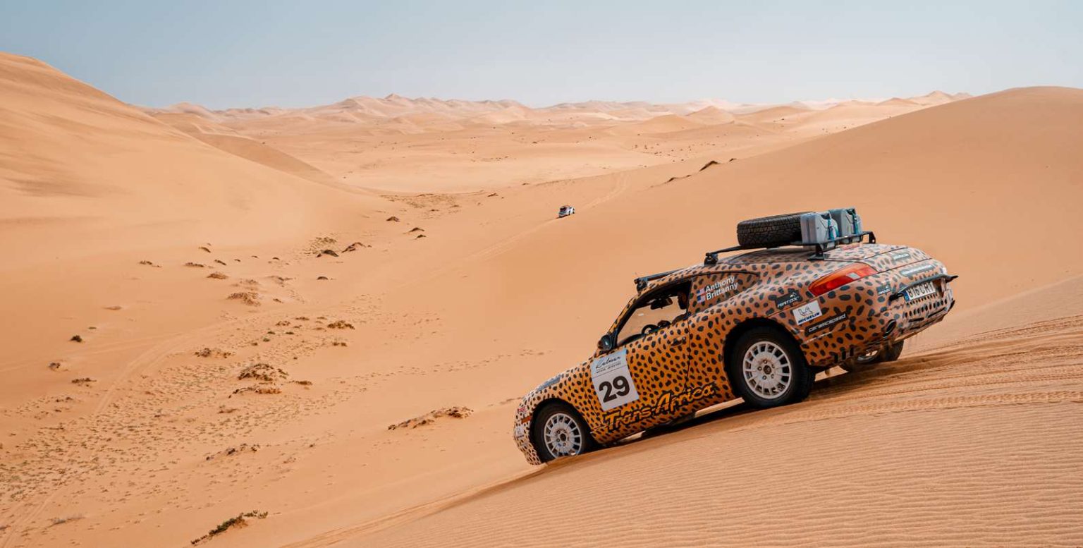 Porsche 911 safari car climbing a red sand dune in Namibia