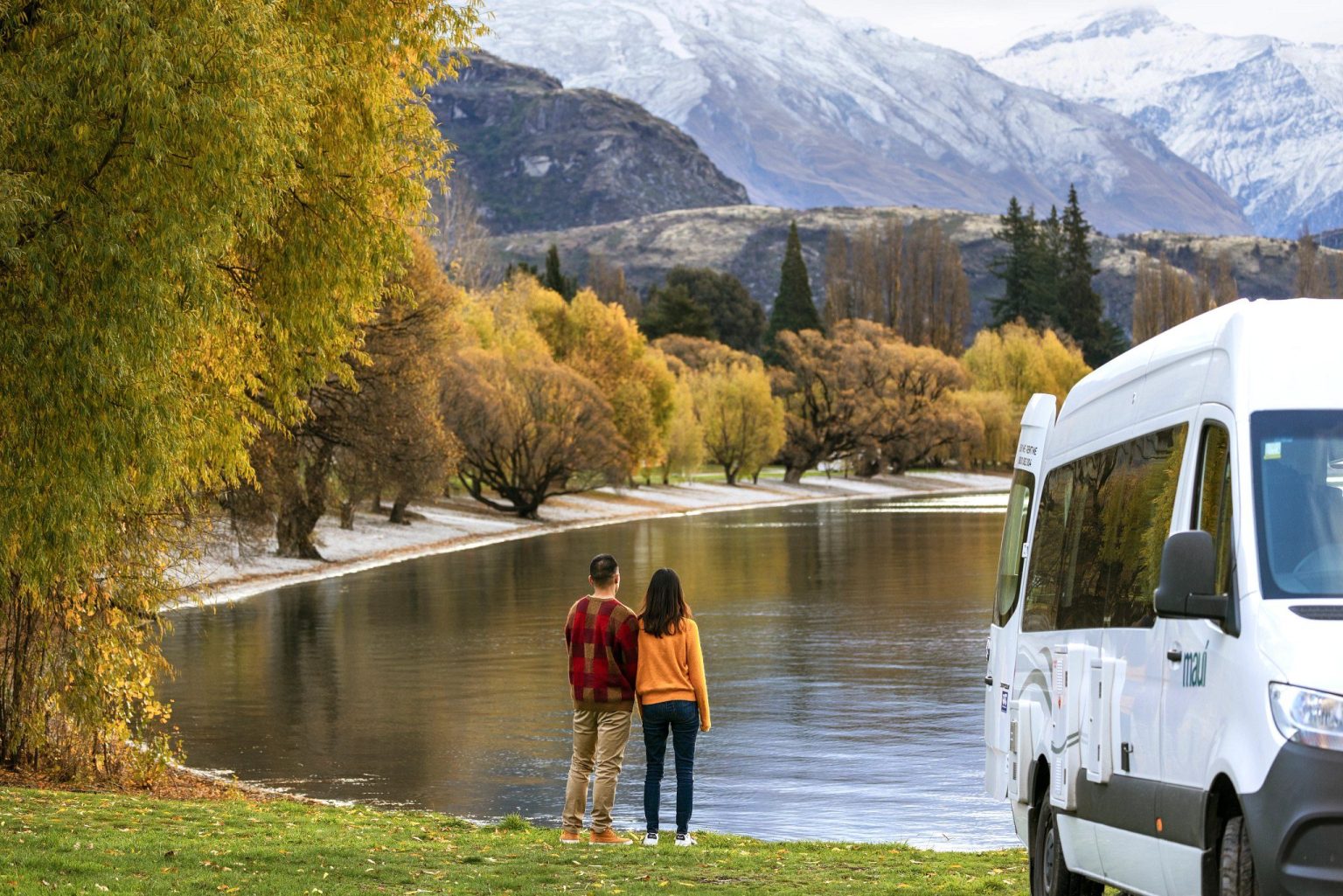 Couple by an autumn lakeside with a campervan and snowy peaks, Lake Wanaka, New Zealand's South Island