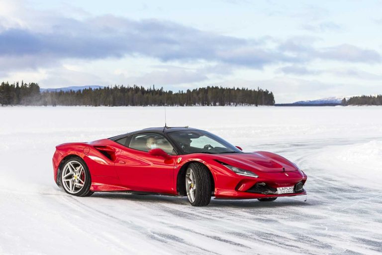 Red Ferrari sports car drifting on a frozen lake with distant pine forest