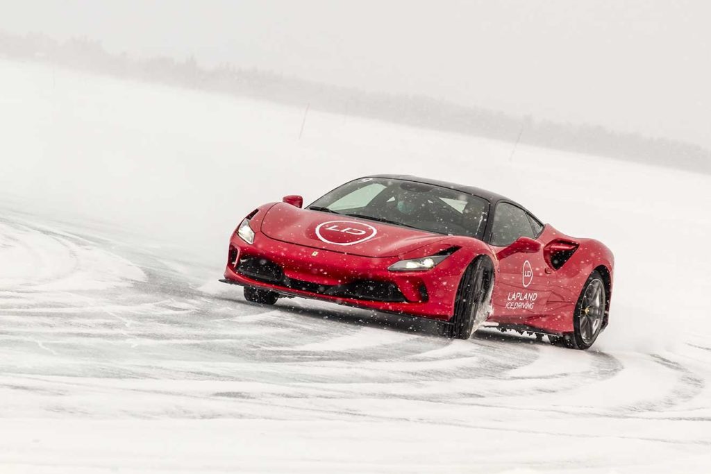 Red Ferrari sports car sliding through a snowy corner on the ice track
