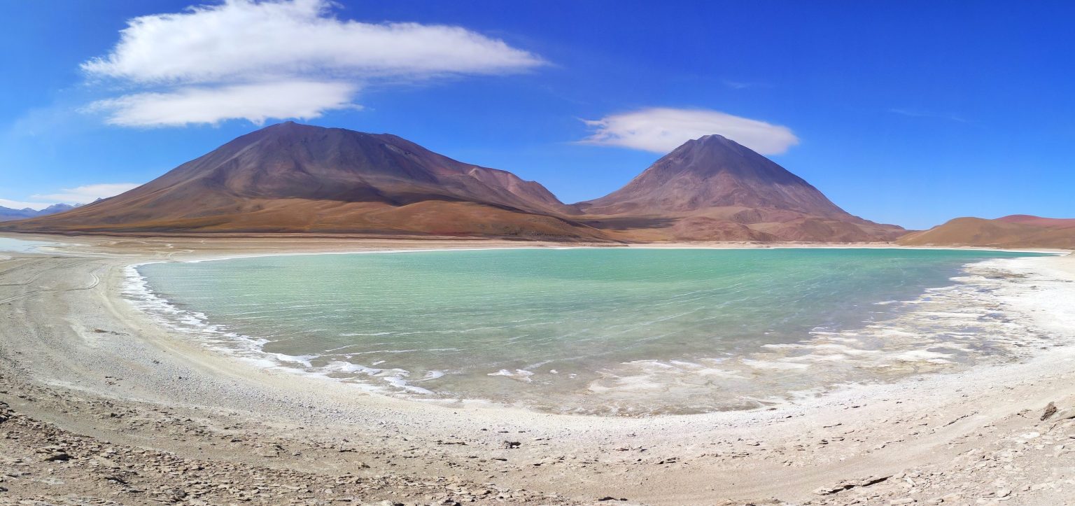 Turquoise lagoon with white salt shore beneath two volcanoes on the Bolivian altiplano