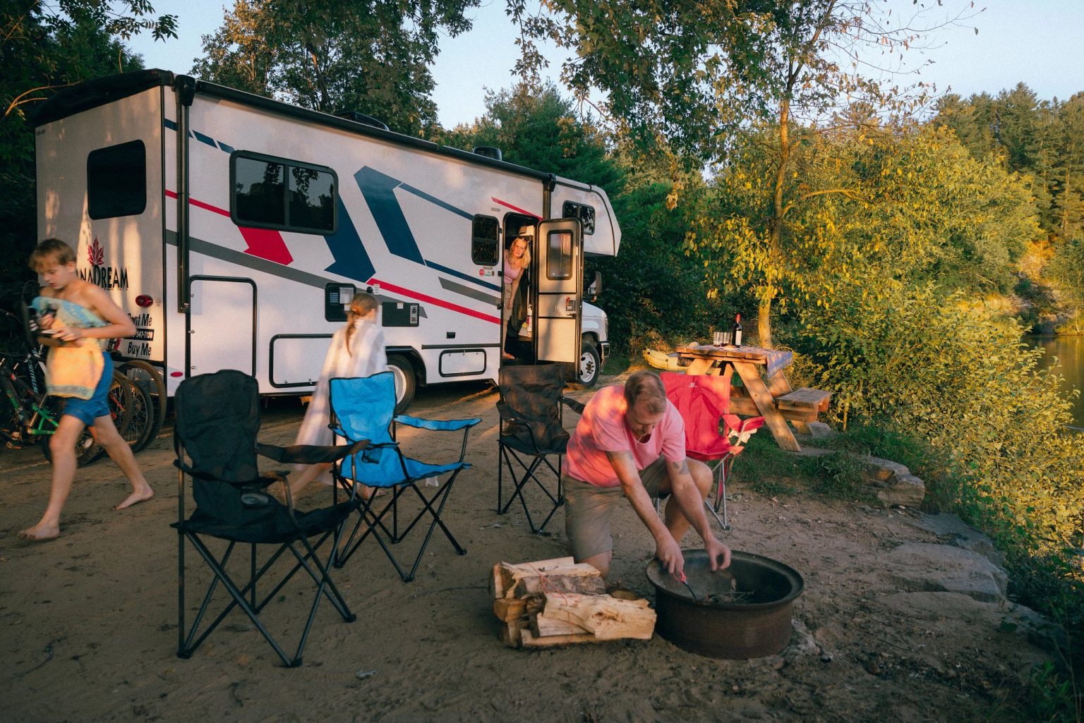Family relaxing by a campfire beside a motorhome, Ontario, Canada