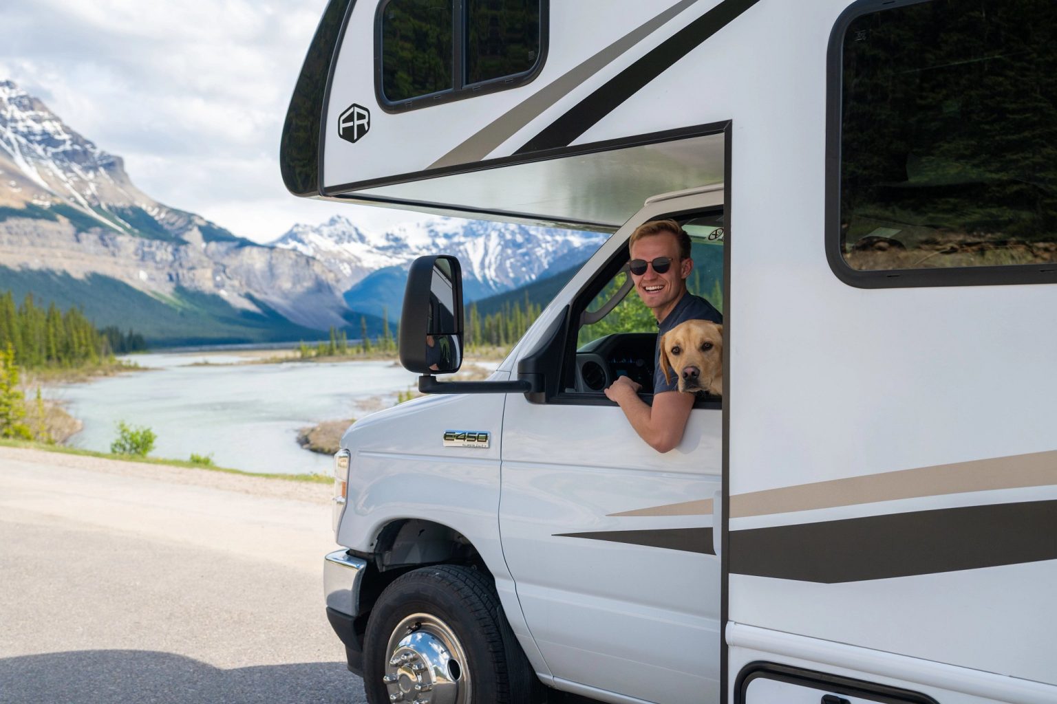 Man and dog in a motorhome cab beside a mountain river, Jasper, Canada