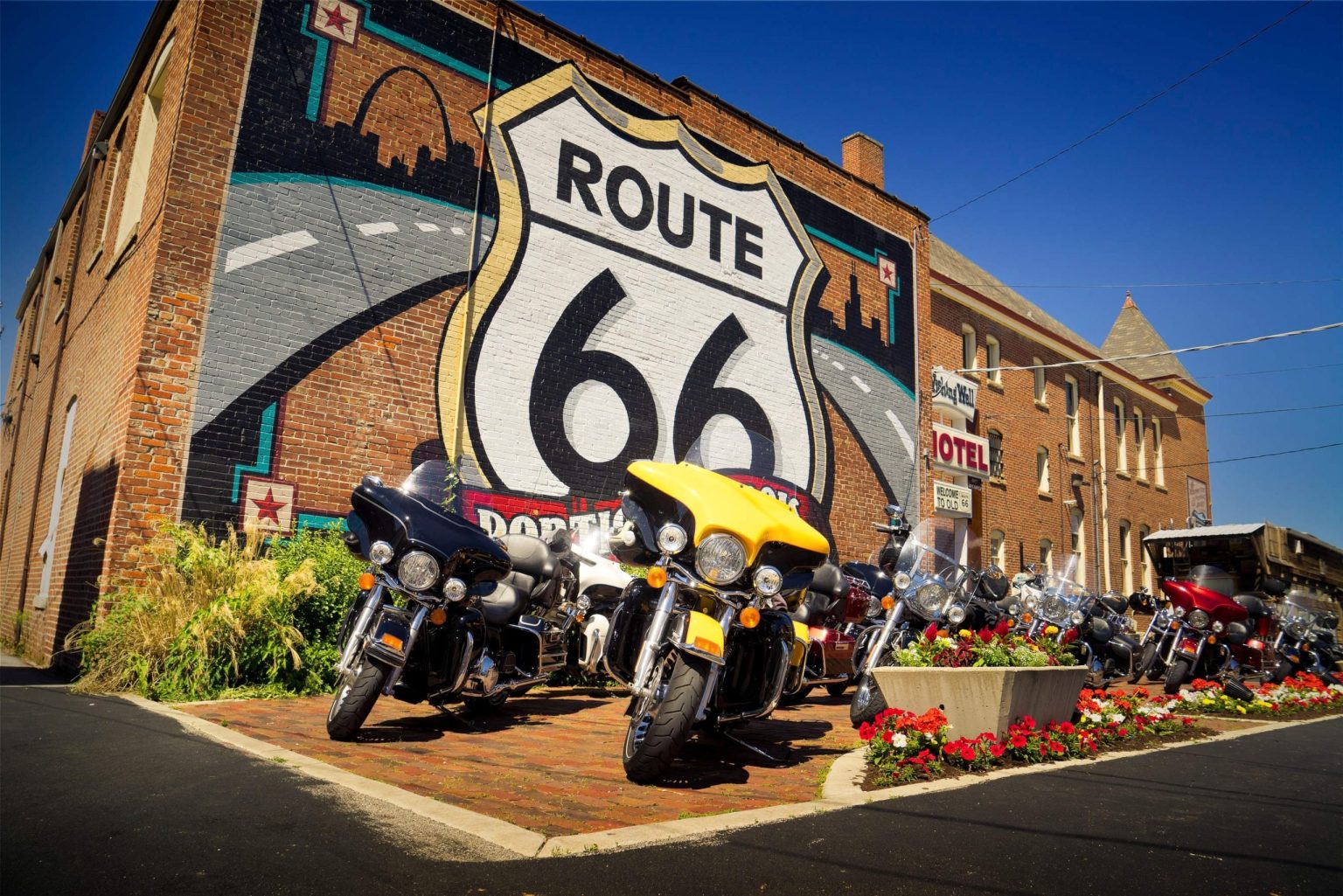 Harley-Davidson touring motorcycles parked beneath a giant Route 66 shield mural