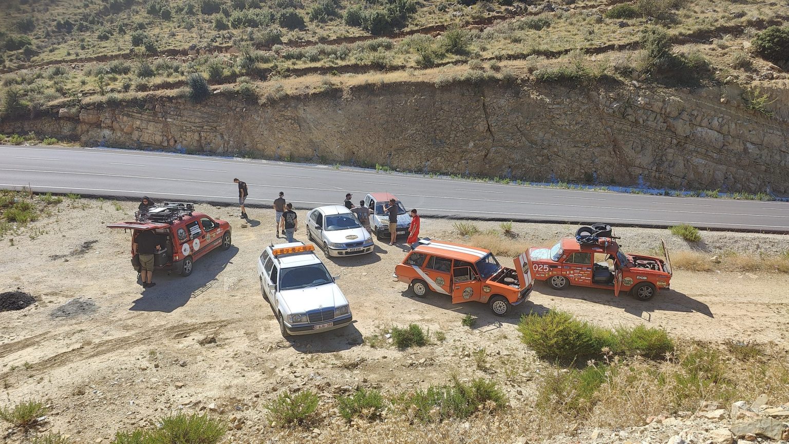 Banger rally cars stopped on a dusty track below a rocky hillside