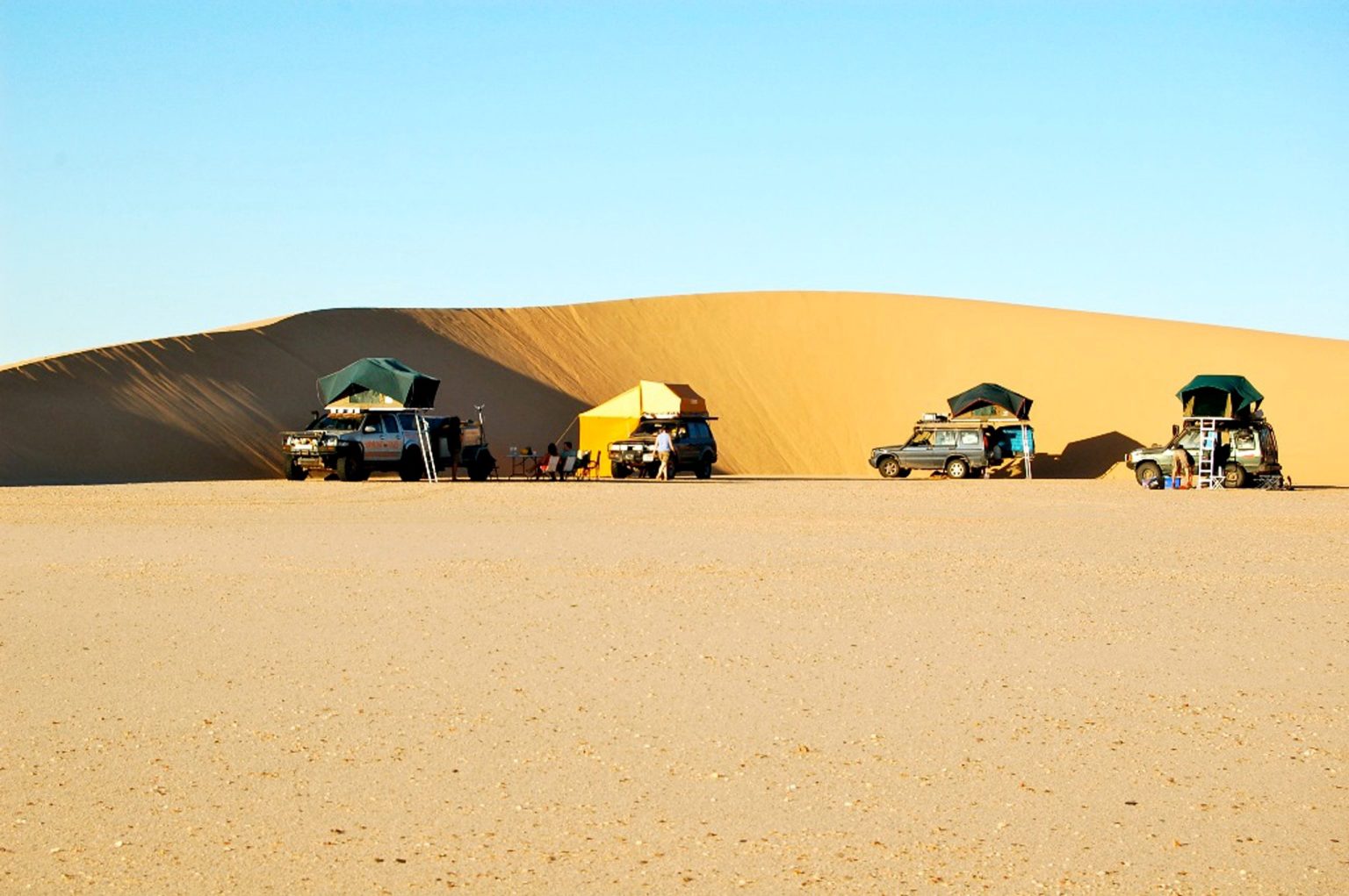 4x4 campers with rooftop tents at a camp below golden Sahara dunes