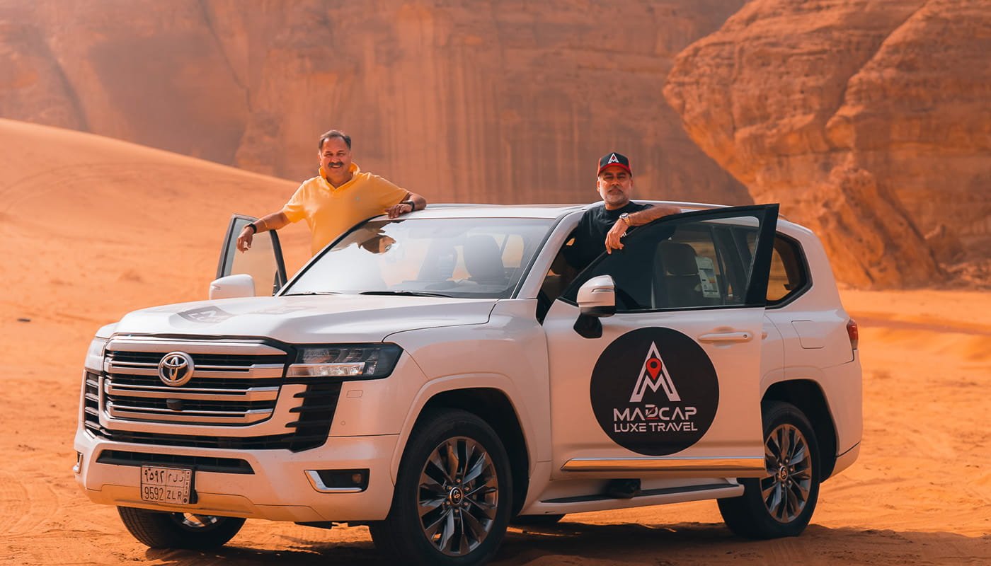 Madcap Land Cruiser and travellers among the red sandstone cliffs of Saudi Arabia