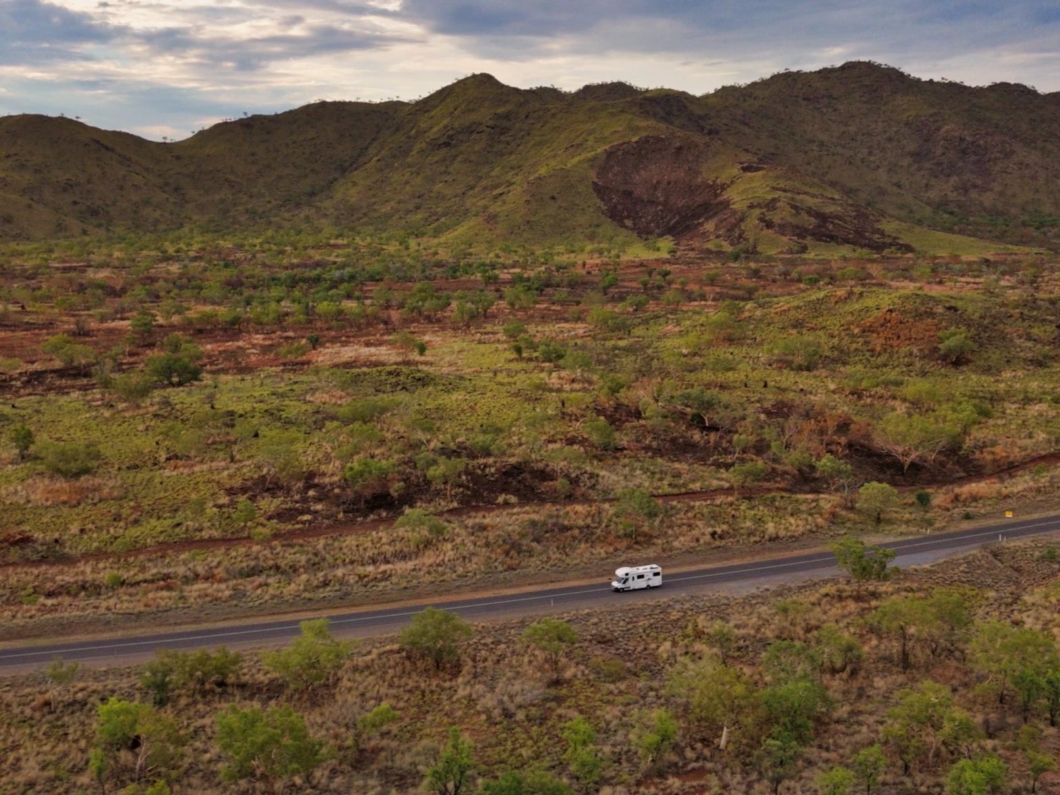 Motorhome on a road through green hills and scrub, on the outback drive to Broome, Western Australia