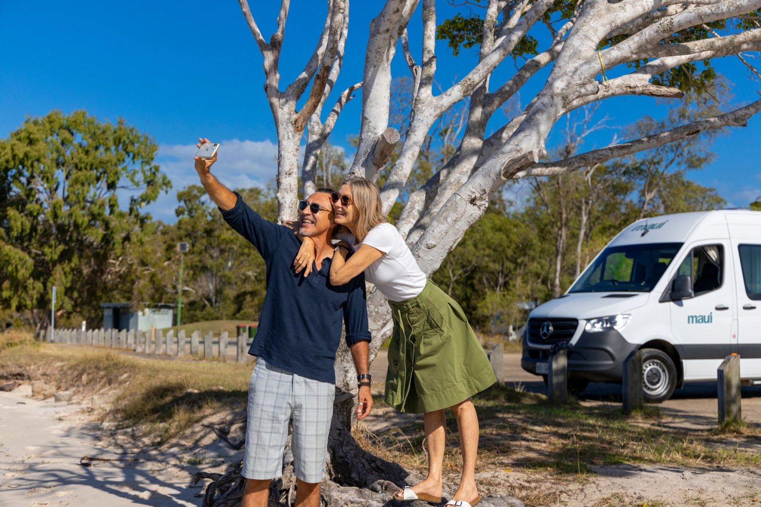 Couple taking a selfie beside a campervan under gum trees