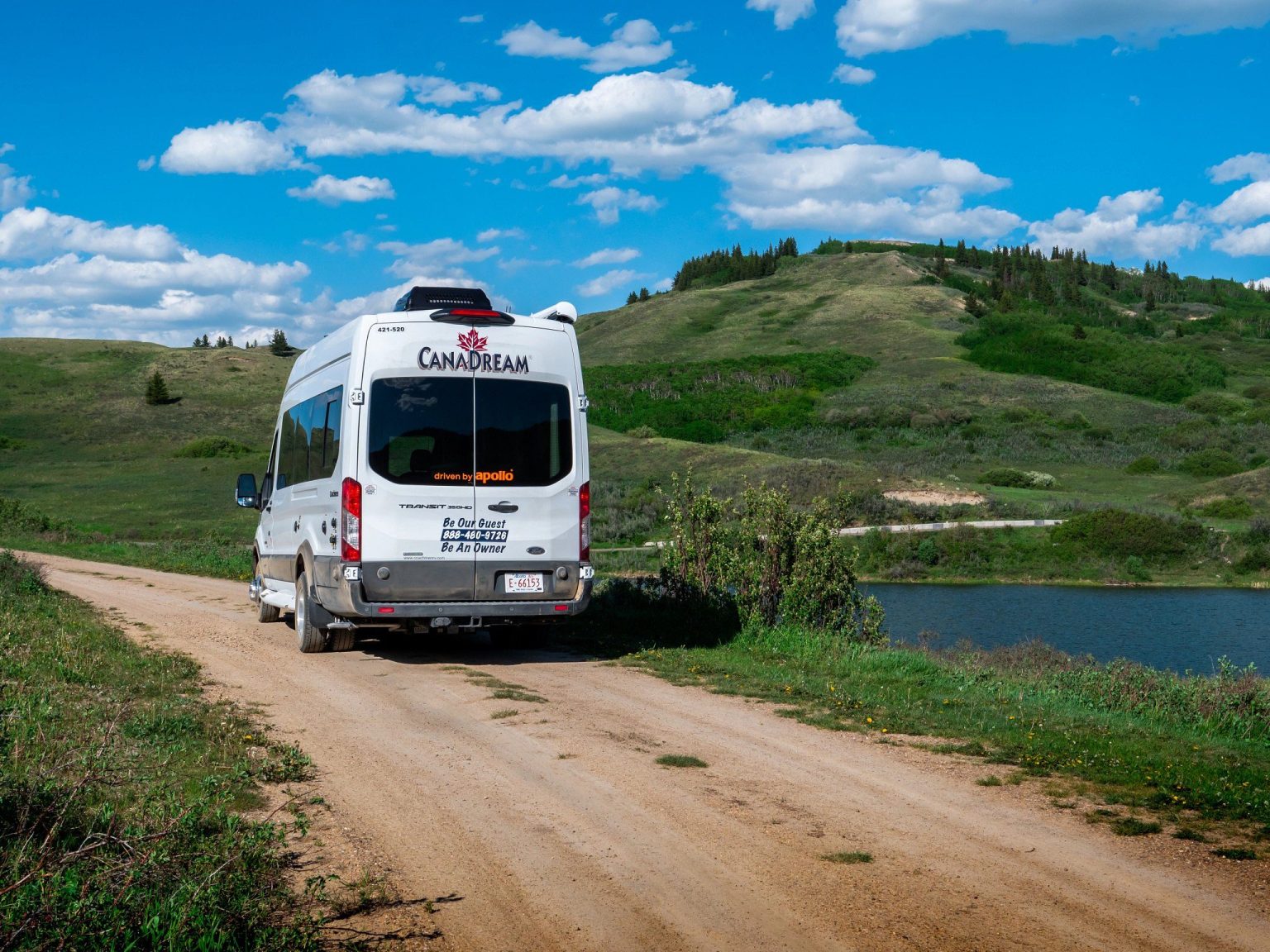 Campervan on a dirt track through grassy hills, Alberta, Canada