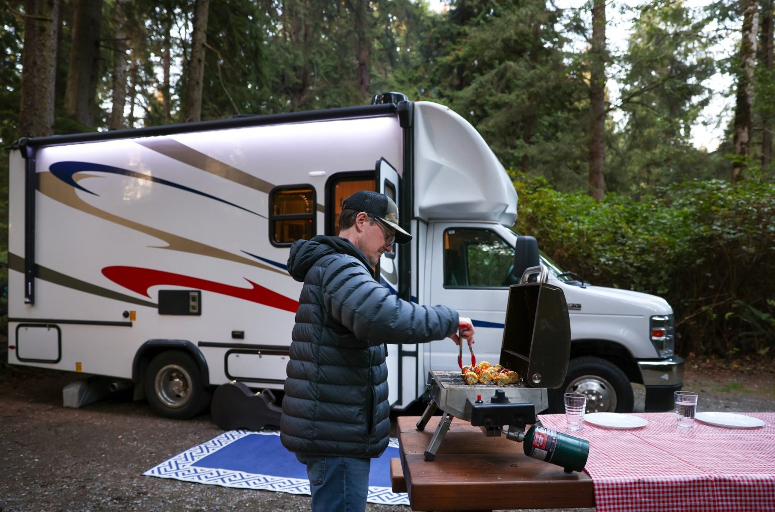 Man cooking at a camp table beside a motorhome in the forest, British Columbia, Canada