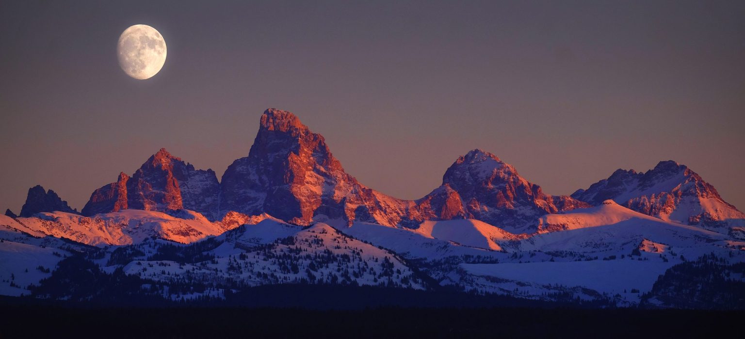 Snow-capped Grand Teton peaks in alpenglow with a rising moon, Wyoming
