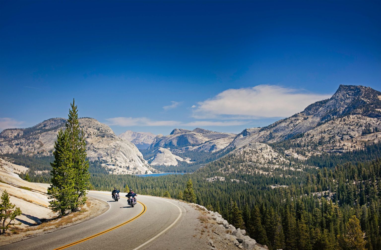 Motorcyclists riding a mountain road past granite peaks in Yosemite National Park